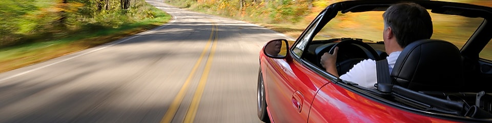 Open top red car driving along a curving country road at speed.,Curving country road at speed.